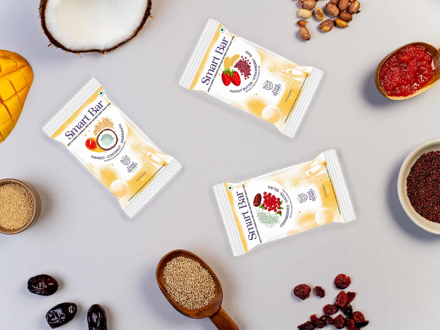 Feed Smart Smart Bars flatlay — three wrapped fruit-and-millet bars surrounded by mango, coconut, dates and grains