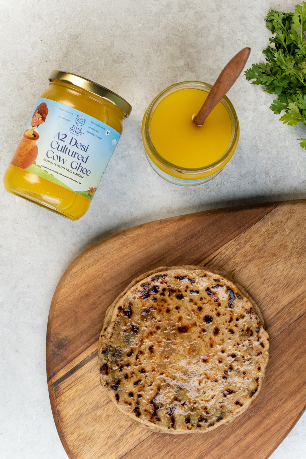 Feed Smart A2 Desi Cultured Cow Ghee with a fresh paratha on a wooden board