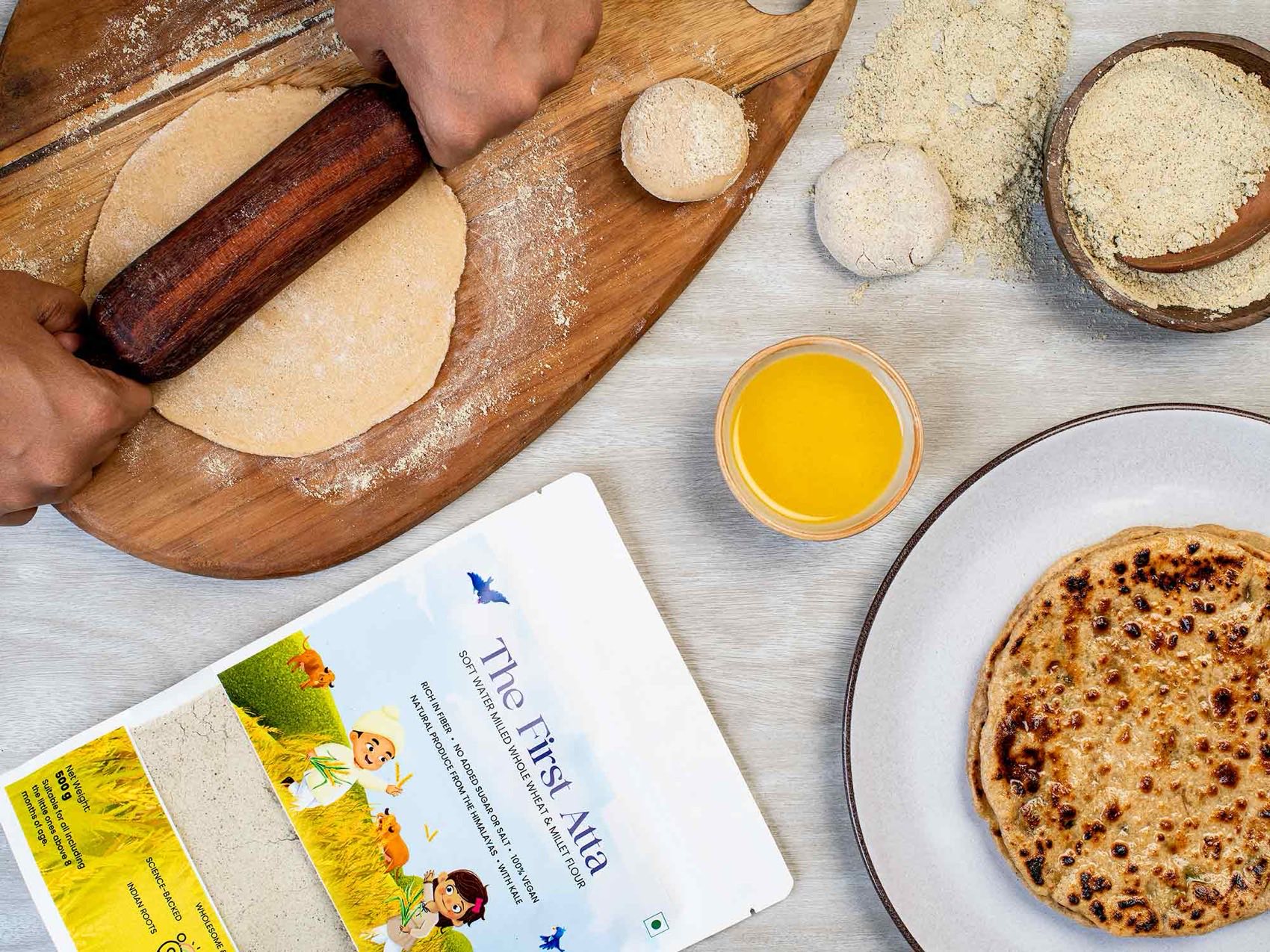 The First Atta in use — fresh parathas, a bowl of ghee, millet flour and hand-rolled dough around the Feed Smart pack